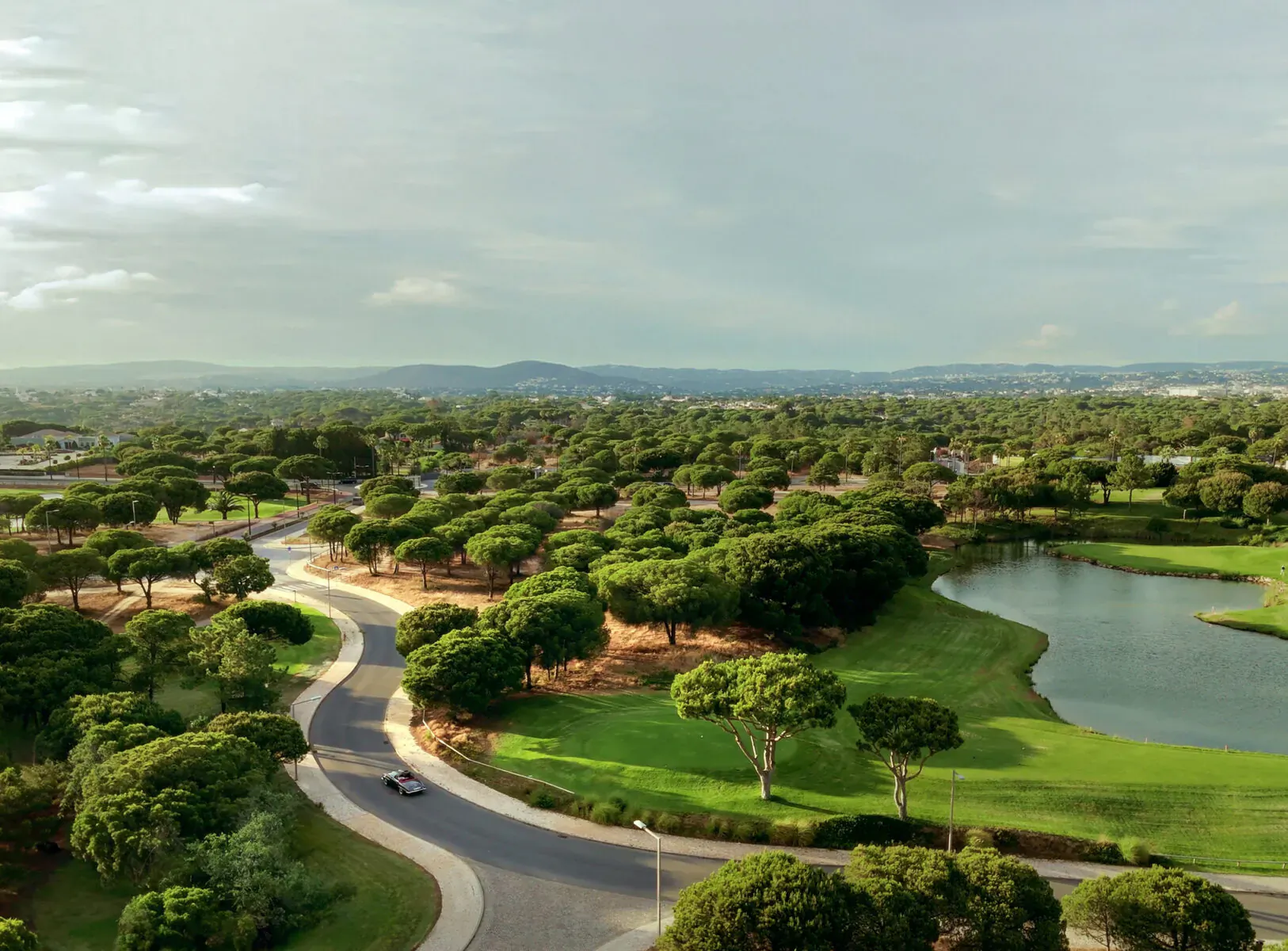 Aerial view of Vale do Lobo Resort, Portugal: lush golf course, winding roads, lake, and branded residences amid trees.