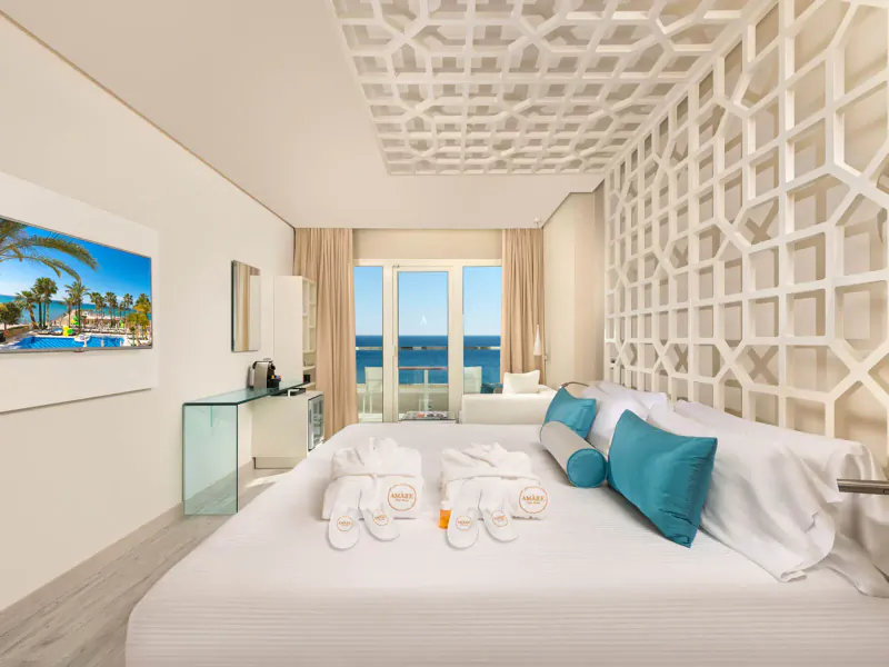 Luxurious Amàre Marbella hotel suite with king bed, beach towels, balcony view of blue sea and palms.