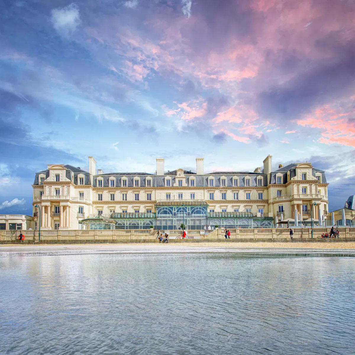 Grand luxury hotel in Saint-Malo, France, by the beach at sunset with people strolling.