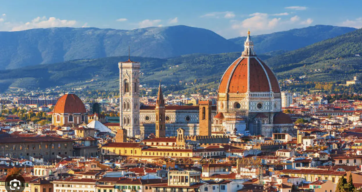 Aerial view of Florence skyline with Brunelleschi's Dome, Giotto's Campanile, and city rooftops against mountains.