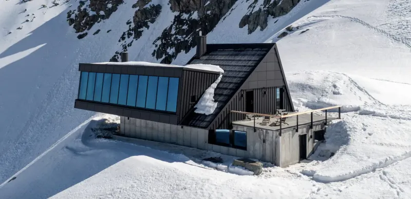 Modern luxury chalet with large blue glass windows and balcony on snowy alpine mountain slope