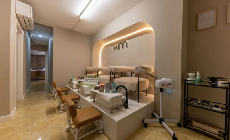 Modern Wumman Spa nail salon interior with curved 'Wumman' sign, beige pedicure chairs, sinks, and products on shelves.