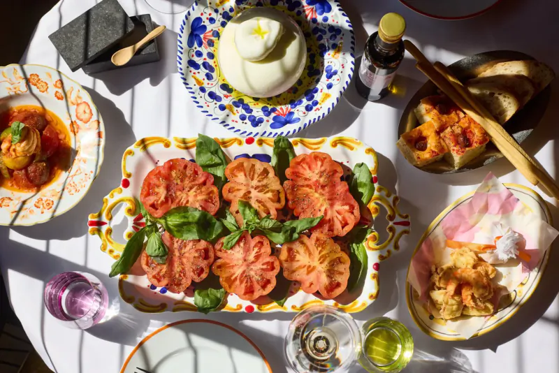 Elegant Italian restaurant table with stuffed tomatoes, burrata, tomato sauce, fried food, wine, and colorful plates.