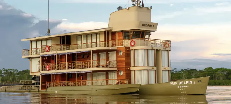 MV Delfin luxury cruise ship with multiple decks docked on river amid Amazon jungle at sunset