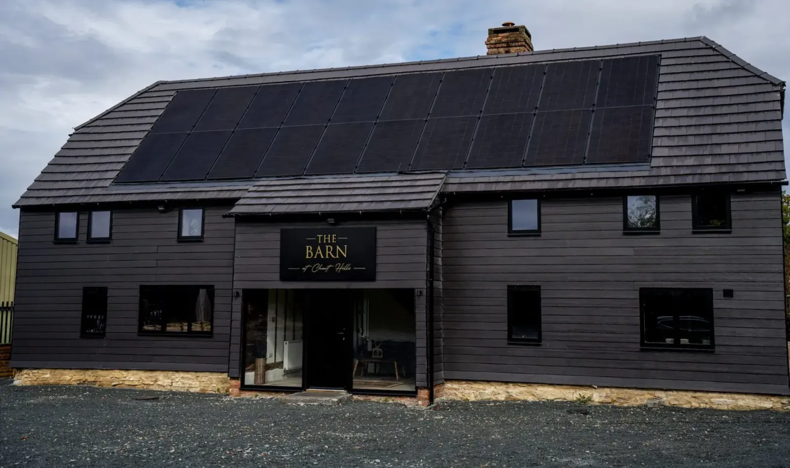 The Barn, a luxurious black barn building with solar panels on the roof and gold sign, at Chart Hills.