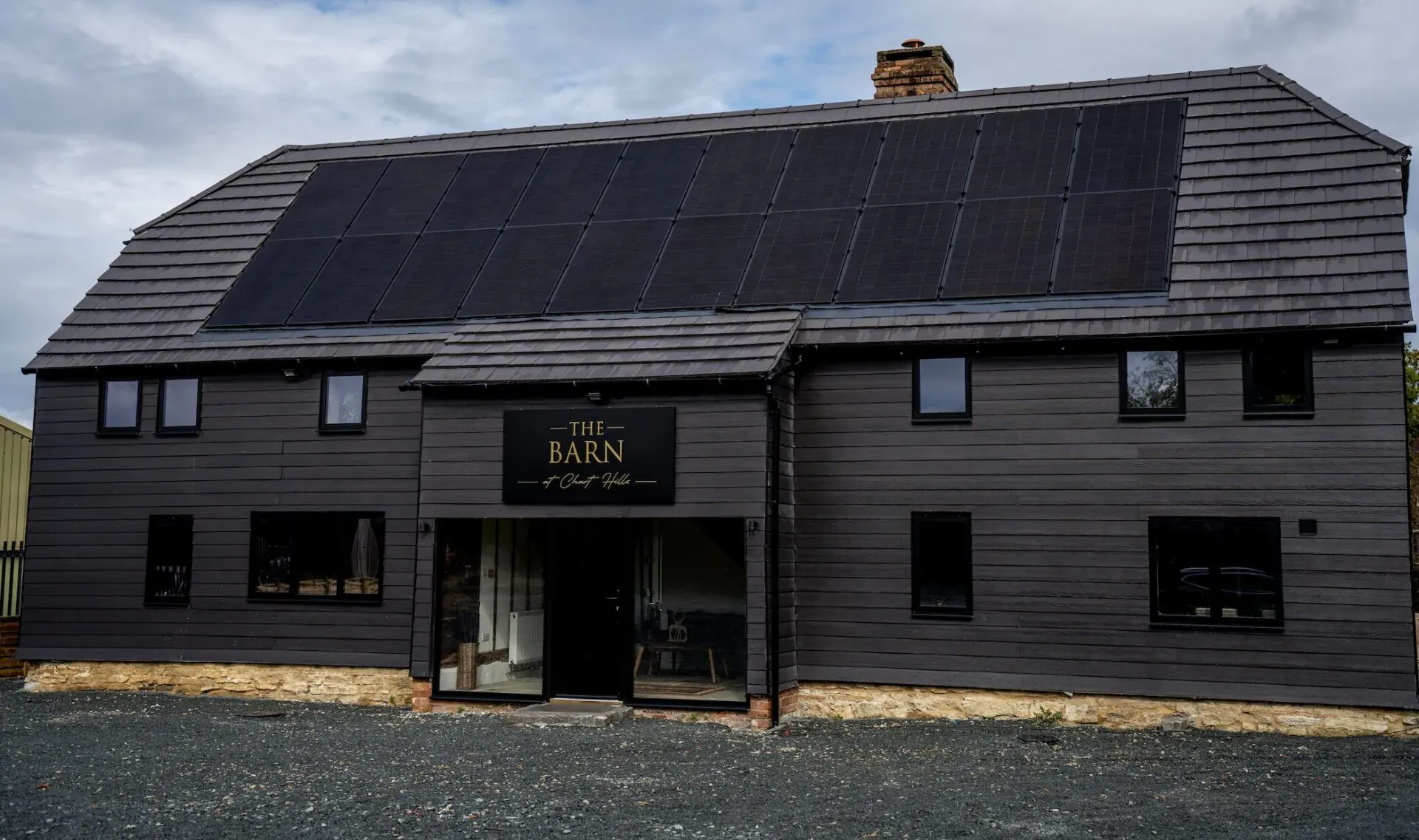 The Barn, a luxurious black barn building with solar panels on the roof and gold sign, at Chart Hills.