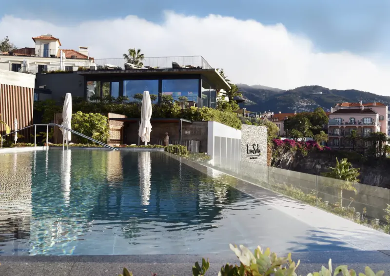 Infinity pool at Les Suites Hotel at The Cliff Bay, Funchal, Madeira, with ocean views, umbrellas, and mountains.