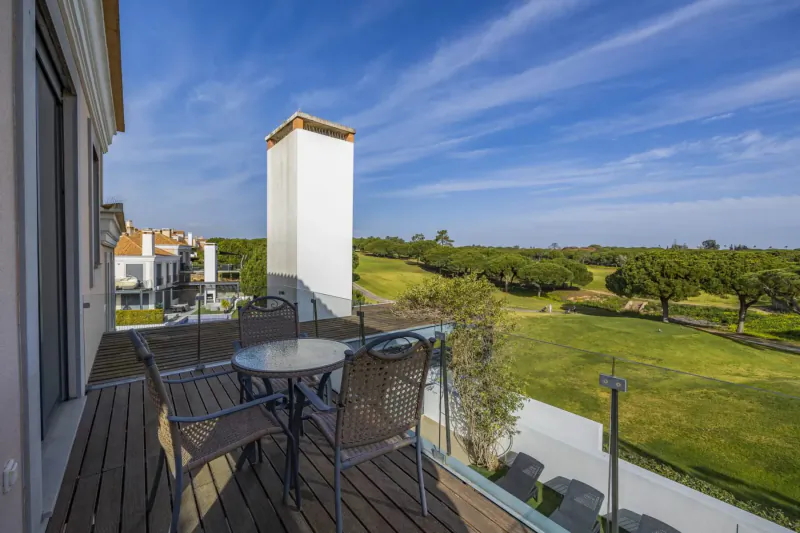 Spacious wooden balcony with table and chairs overlooking lush green golf course at Vale do Lobo resort, Portugal
