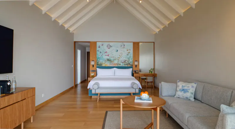 Spacious Amari Maldives villa with king bed, ocean mural headboard, sofa, coffee table, and wooden floors