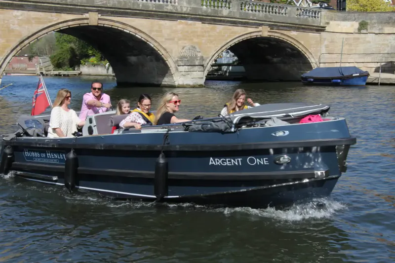 Regent One boat with smiling passengers under stone bridge on river, Hobbs of Henley.
