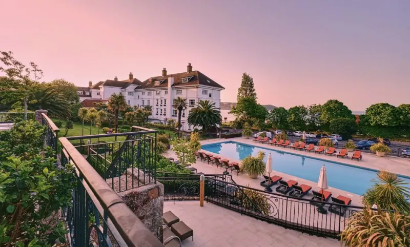 St. Brelade’s Bay Hotel in Jersey at sunset, with outdoor pool, orange loungers, palm trees, and lush gardens.