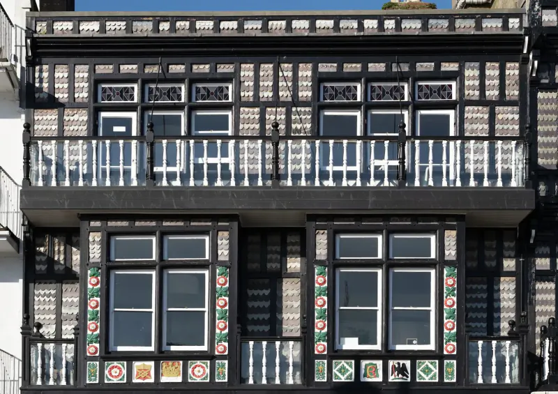 Close-up of ornate black-and-white half-timbered building facade with decorative green floral window surrounds and balconies.