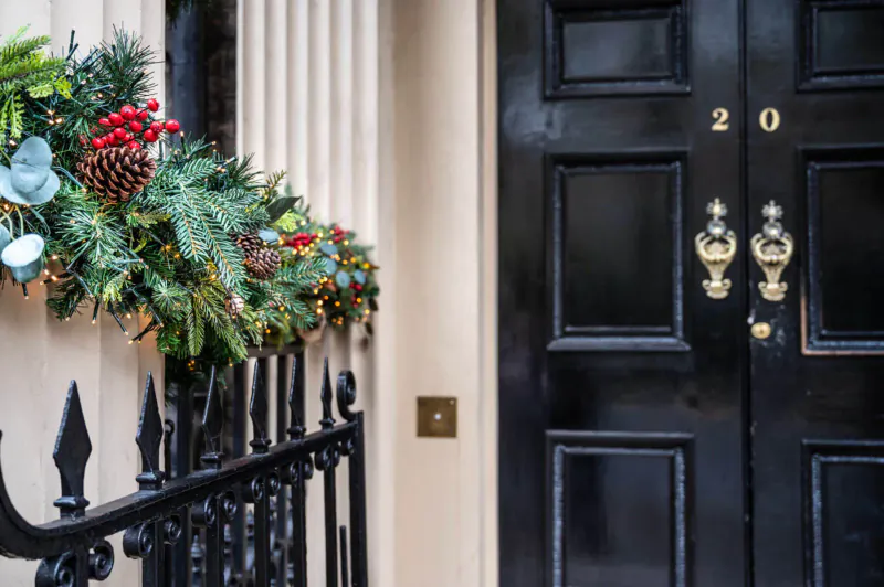 Festive Christmas wreath on black door numbered 20 at Home House, London, with railing and garlands.