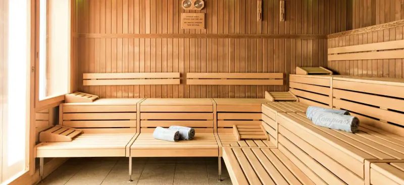 Wooden sauna interior with tiered benches, white towels folded on seats, and wall clock in luxury alpine hotel.