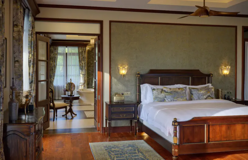 Luxurious bedroom in La Cigale Estate, Seychelles, with wooden four-poster bed, ceiling fan, and en-suite bathroom visible through open doors.