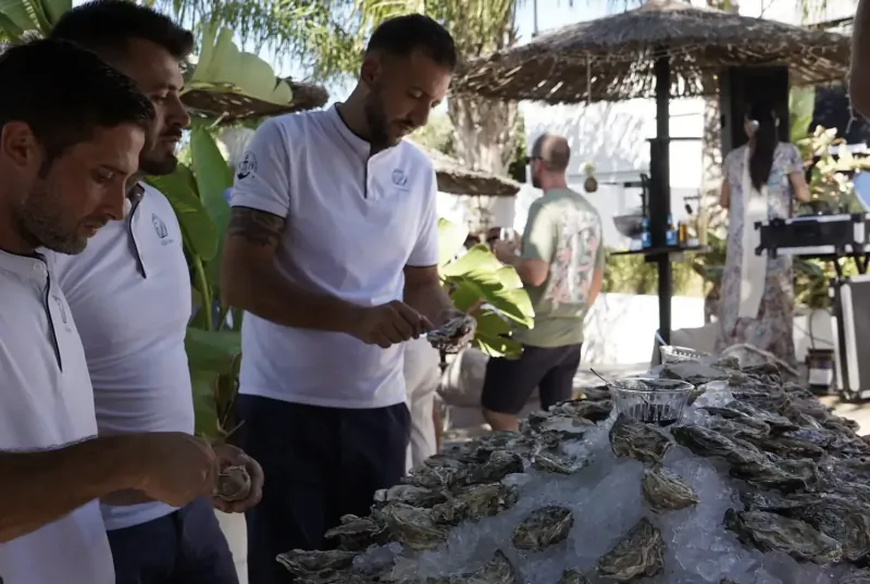 Sam Mead and men in white polos shuck and handle fresh oysters on ice at beachside hotel restaurant