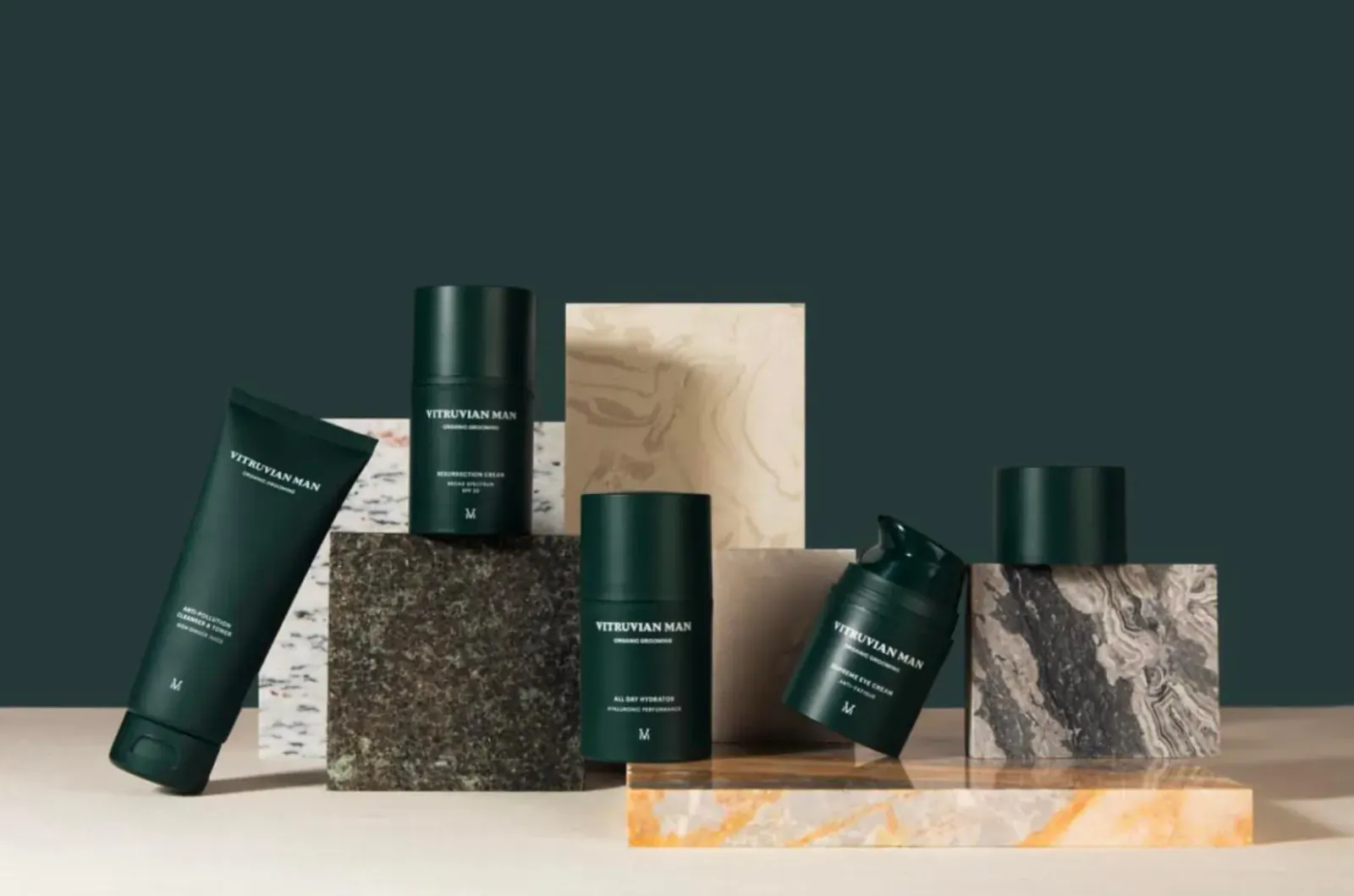 Assortment of green Luxuria Homme skincare products on stone pedestals against dark green backdrop
