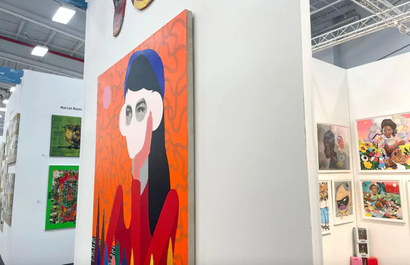 ArtExpo Dallas gallery booth with abstract orange portrait of woman in black hair and orange turban amid colorful paintings