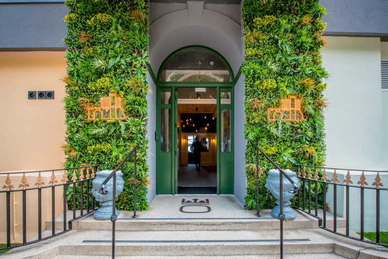 The Imperial Hotel entrance in Tenby, arched green door flanked by lush green walls, orange logo signs, blue pots, and steps.