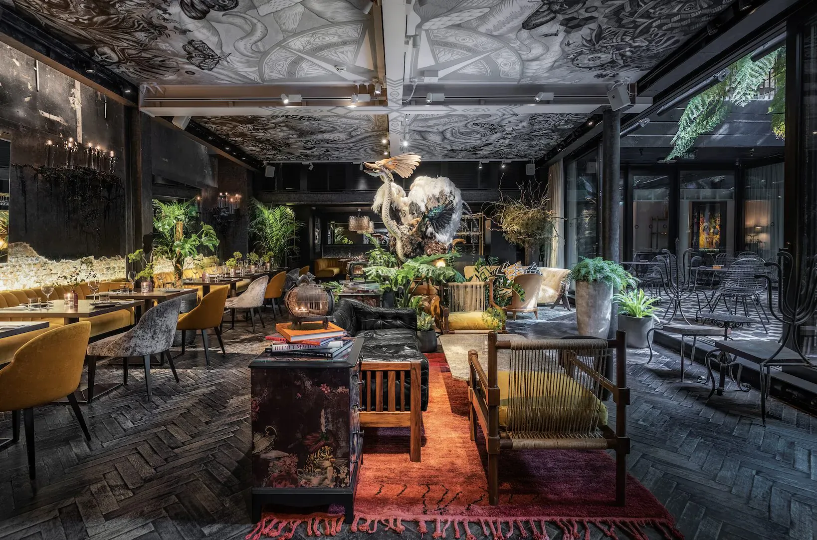 Luxurious hotel lounge at The Mandrake, London: ornate ceiling, skeleton sculpture, plush chairs, plants, bar.