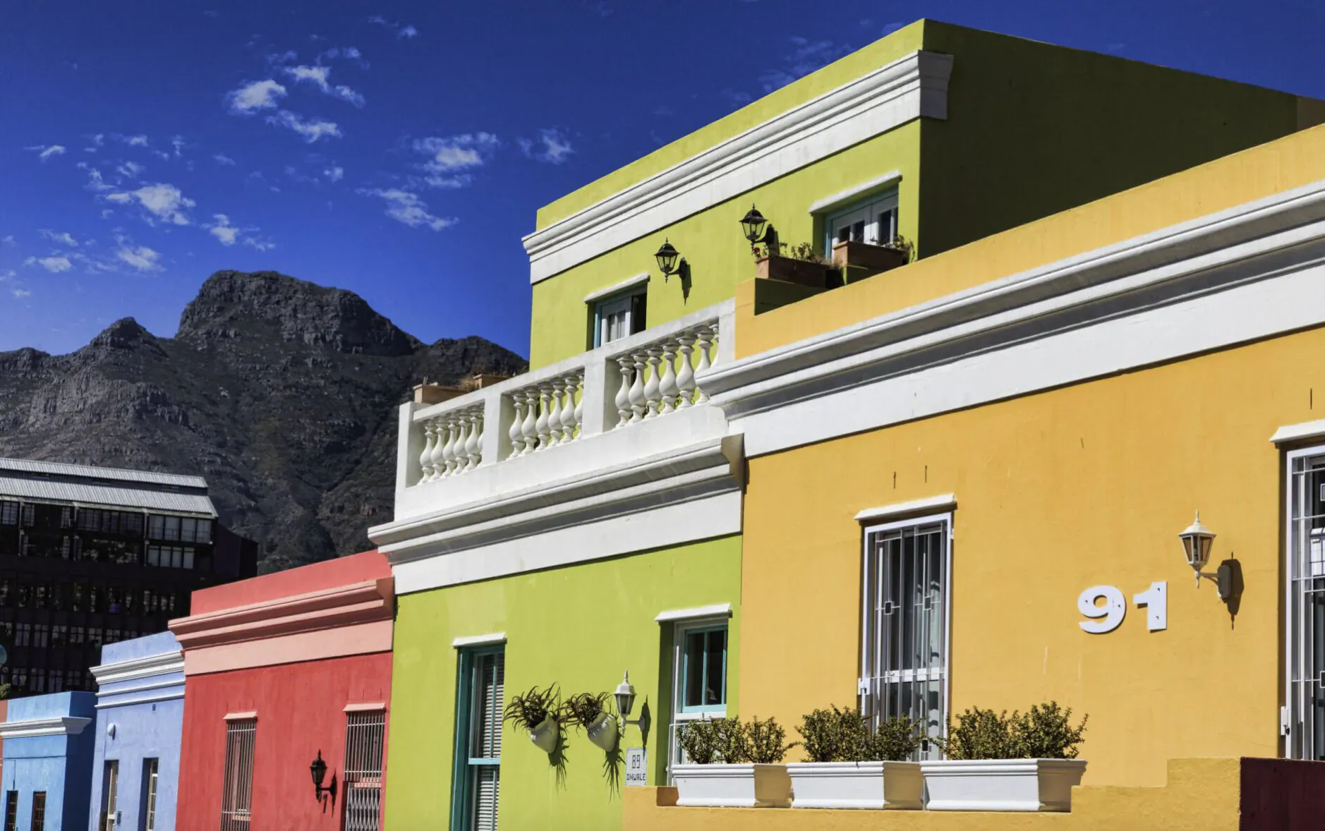 Colorful Bo-Kaap houses in Cape Town: yellow building numbered 91 with green trim, pink neighbor, mountain backdrop.