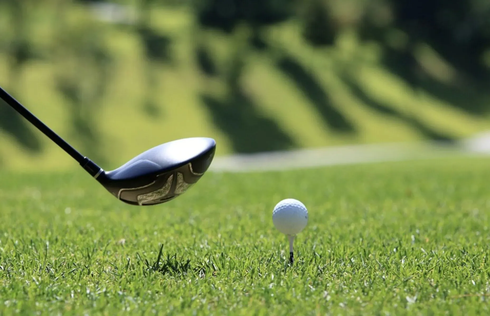 Golf driver club swinging towards a white ball on tee on lush green fairway with rolling hills