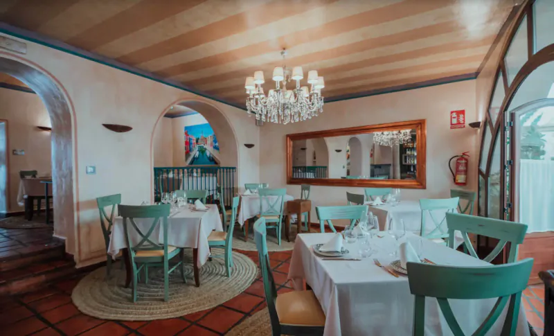 Elegant Italian restaurant interior with arched doorways, chandelier, wooden beams, green chairs, white tablecloths, and set tables.