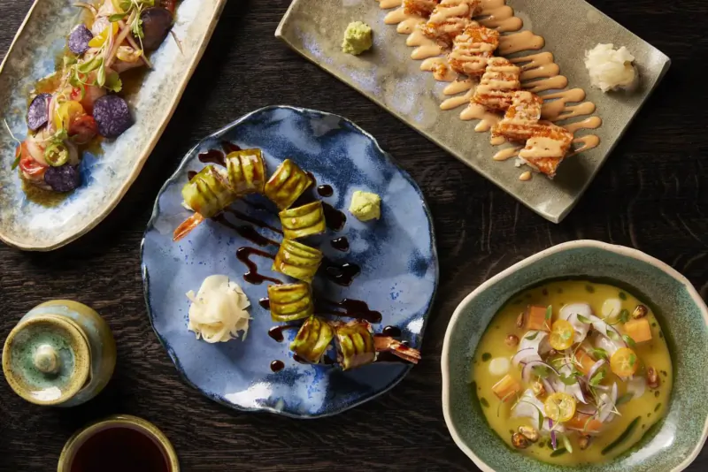 Assortment of sushi rolls, sashimi, ceviche soup, and sake on plates at Chotto Matte Soho