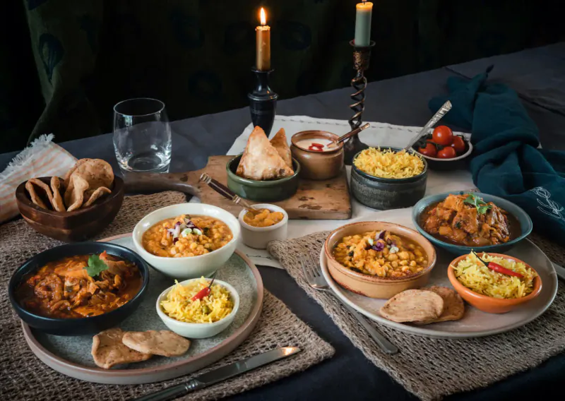 Assortment of Indian dishes on a candlelit table: curries, rice, naan, and chutneys from Mandira’s Kitchen.