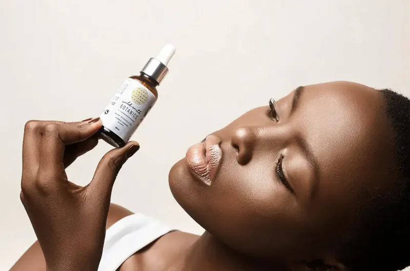 Close-up of Black woman holding Wild Earth Botanics oil dropper bottle to her glossy lips
