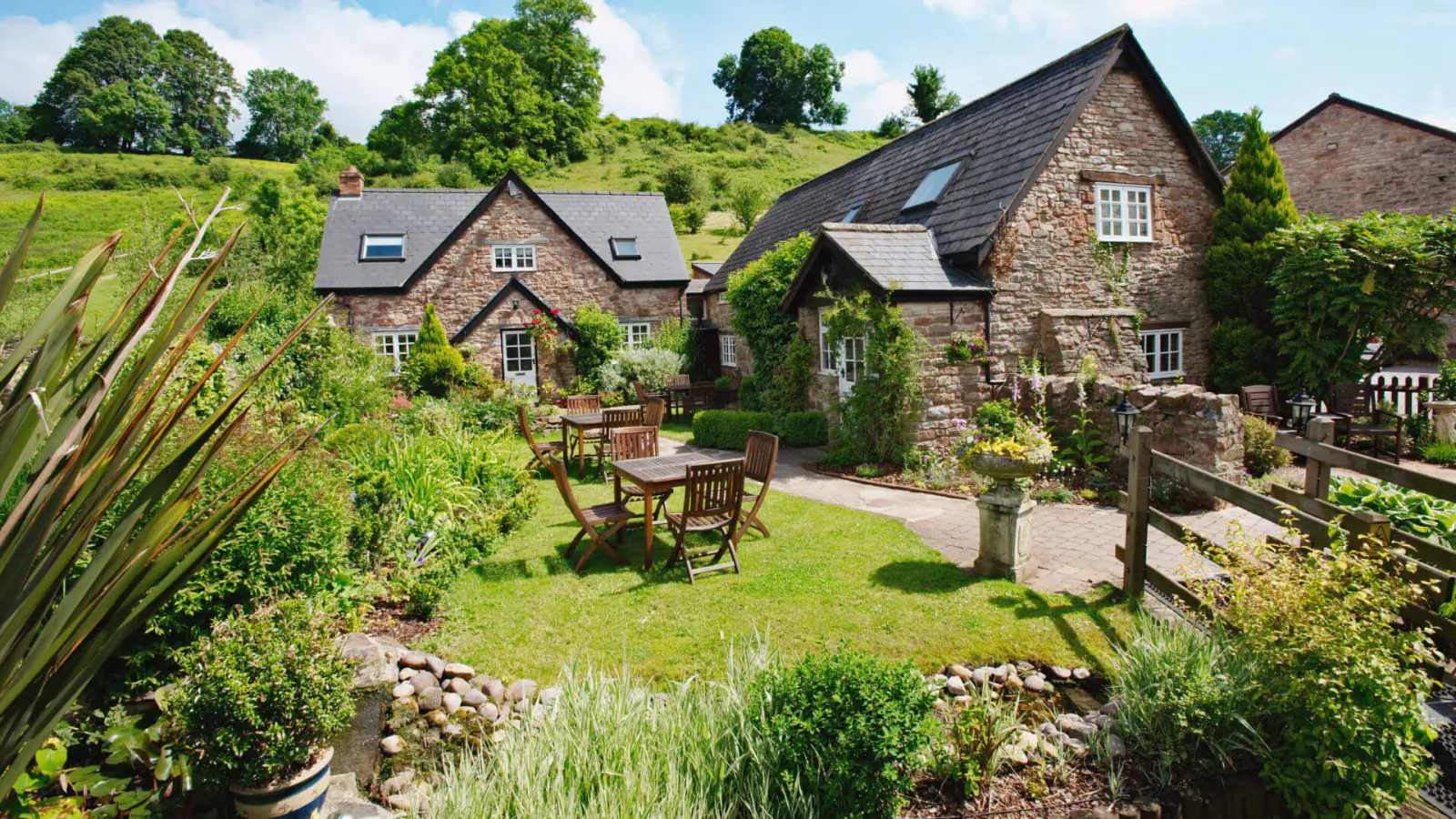 Tudor Farmhouse boutique hotel: stone cottages, garden patio with table, lush greenery in Forest of Dean hills.