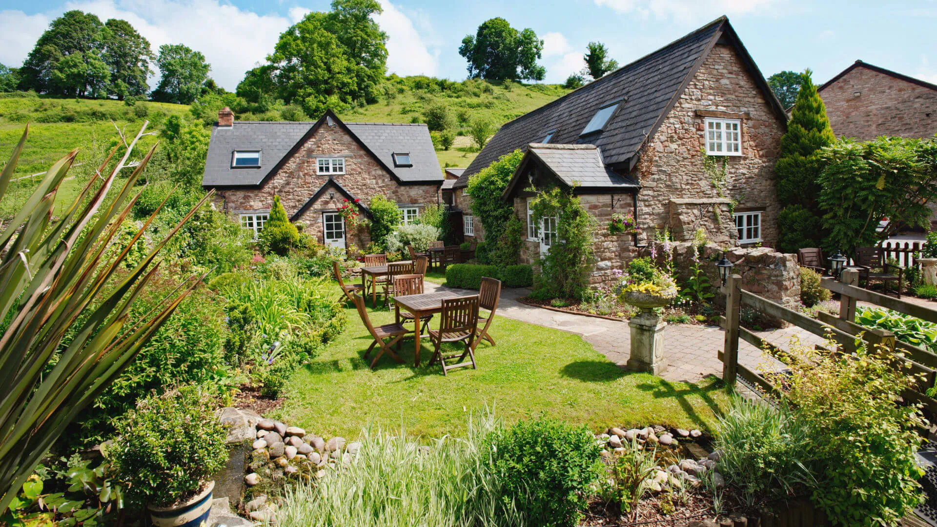 Tudor Farmhouse boutique hotel: stone cottages, garden patio with table, lush greenery in Forest of Dean hills.