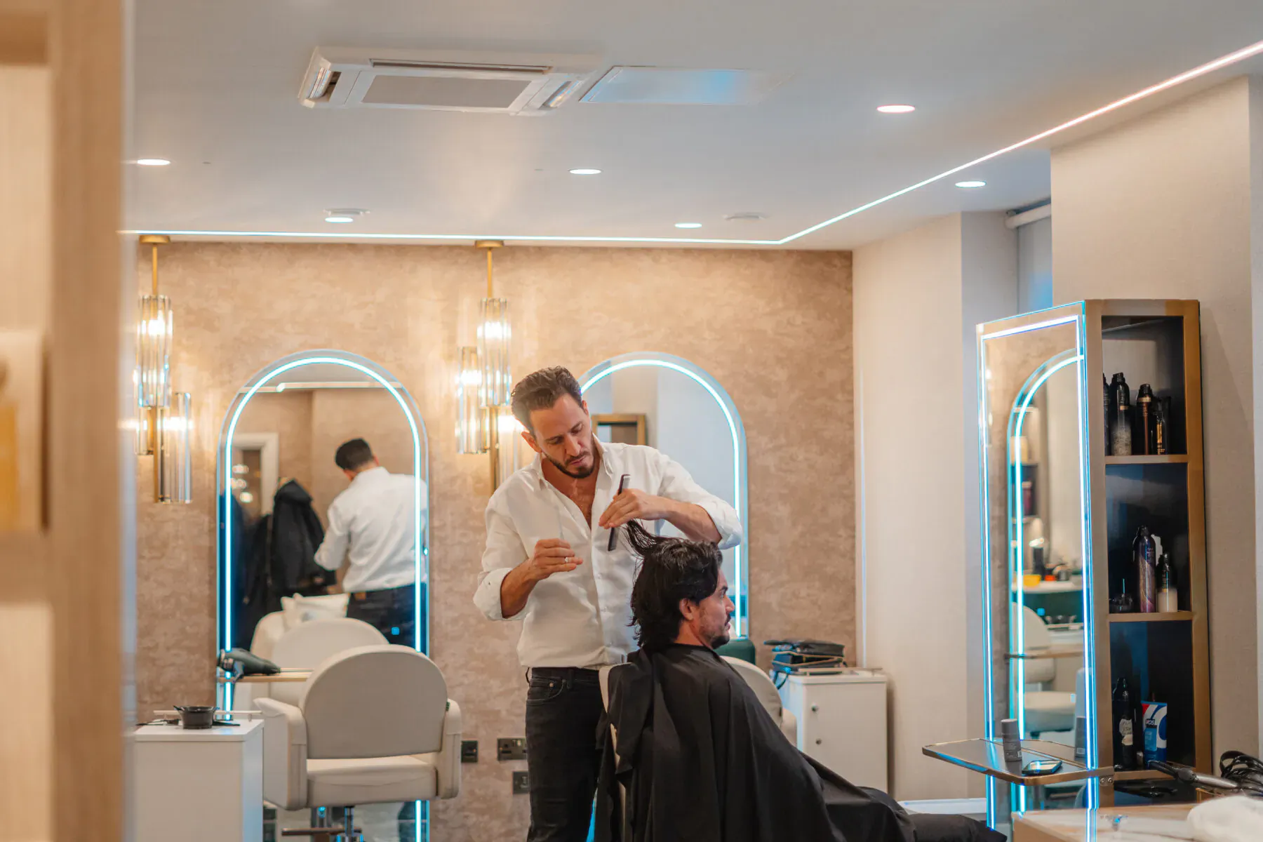 Stylist cutting a client's hair in a luxury salon with arched mirrors and neon accents