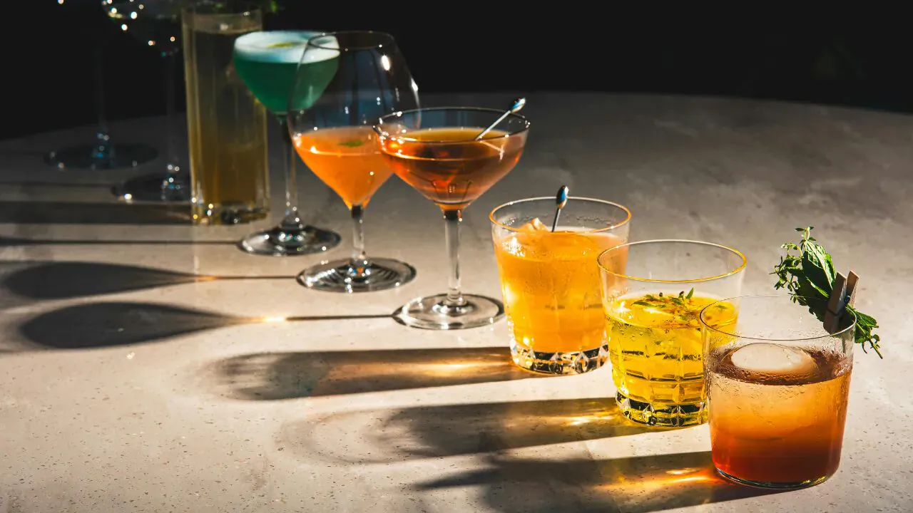 Variety of colorful non-alcoholic cocktails in glasses on table with shadows, garnished with herbs.