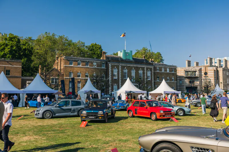 Concours d'elegance: Classic cars displayed on lawn before brick mansion with white tents and crowd