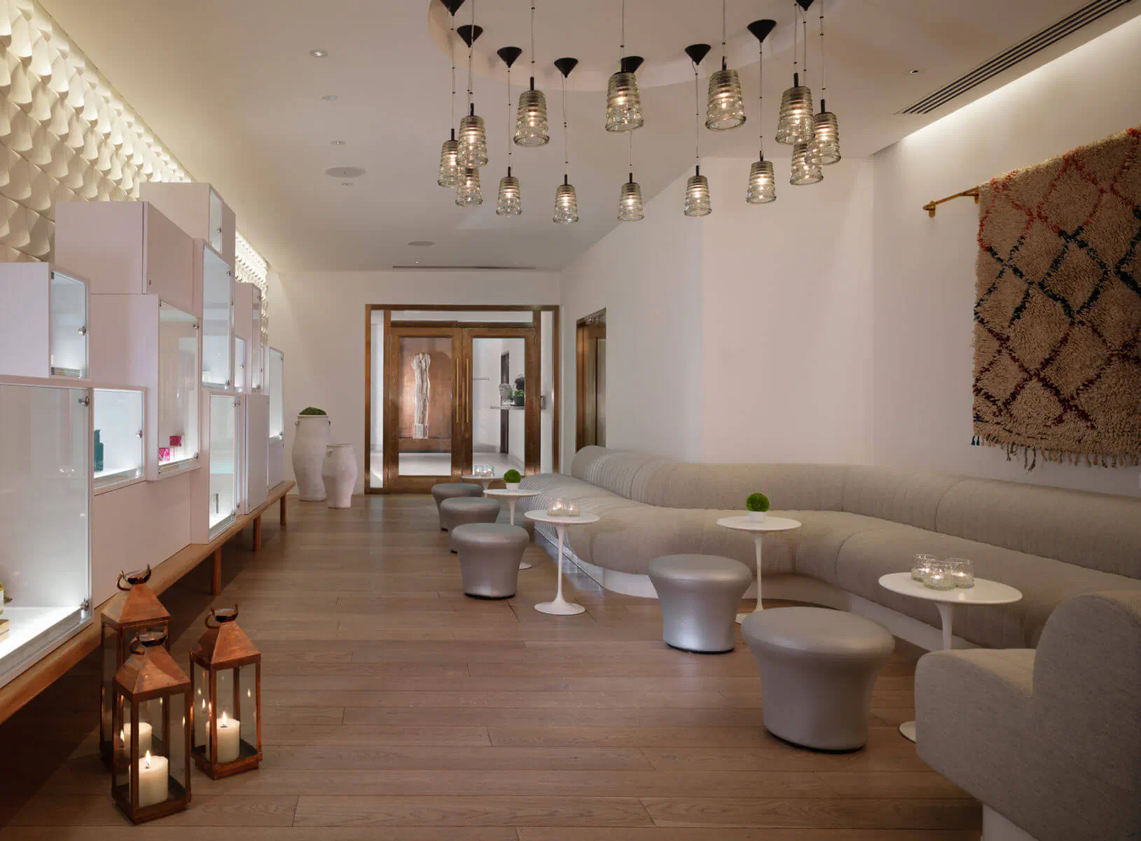 Elegant spa lounge at Sea Containers London with white shelving, curved gray sofa, pendant lights, and woven wall art.