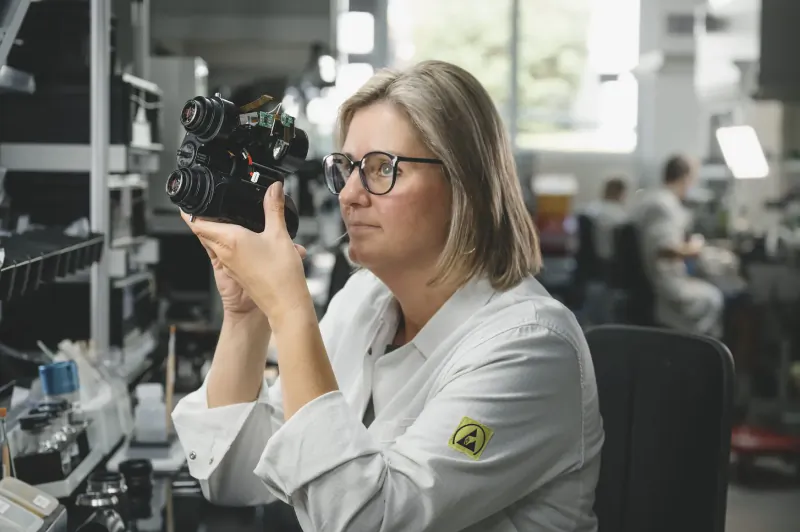 Woman in lab coat holding and inspecting smart binoculars in factory workshop