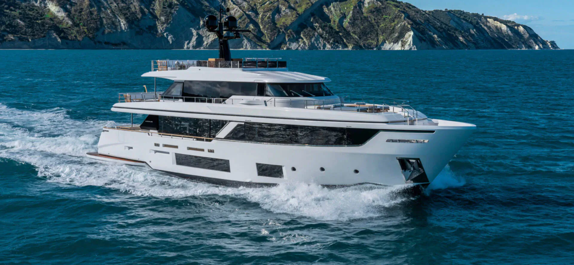 White luxury Ferretti yacht speeding on blue sea with green cliffs in background