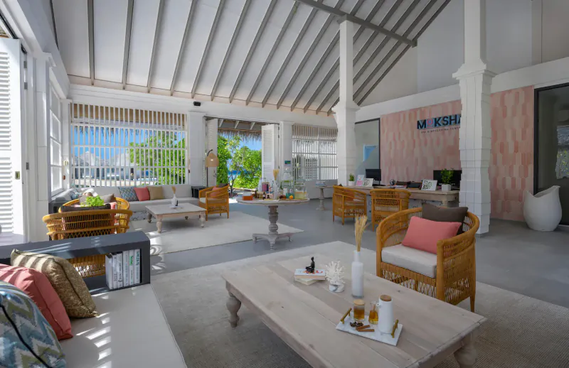 Spacious open-air lobby at Cora Cora Maldives with rattan furniture, ocean view, and 'MK' sign.
