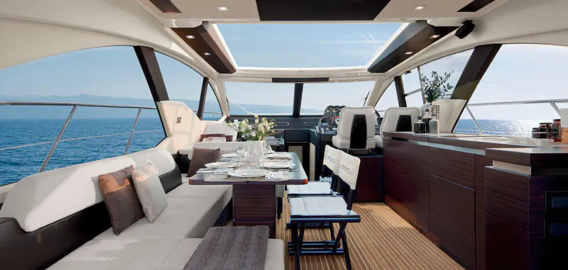 Luxurious modern yacht interior with helm, white leather seating, dining table, and sea view through panoramic windows.