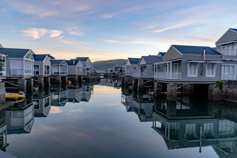 Row of luxury waterside houses on stilts reflected in calm canal at sunset, Turbine Boutique Hotel architecture gallery.