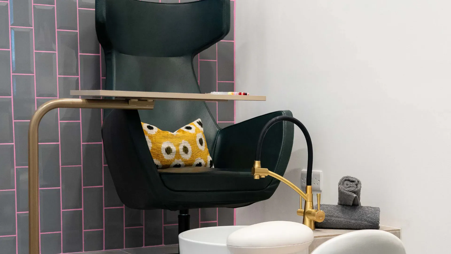 Modern green pedicure chair with yellow floral pillow, gold faucet, white basin in pink tiled salon