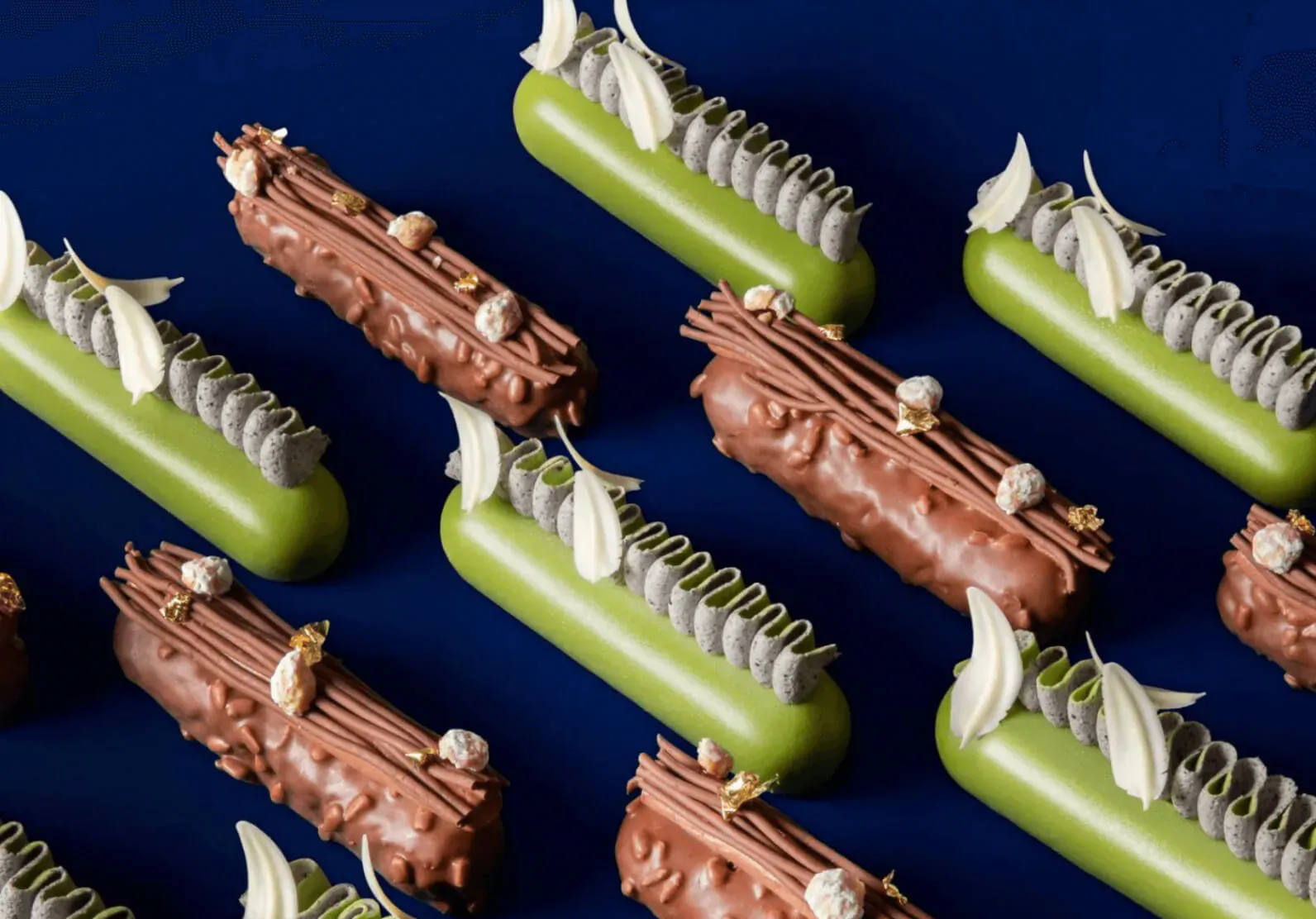 Arranged green and chocolate pastries with nuts and white garnishes on navy background