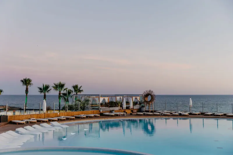 Twilight infinity pool at Vale do Lobo resort, Portugal, with white loungers, palms, and ocean horizon.