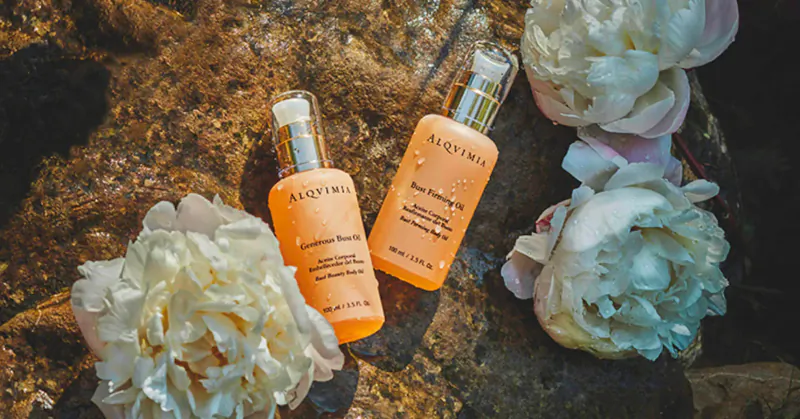 Two Alqvimia orange flower beauty essence bottles on rock with white peonies