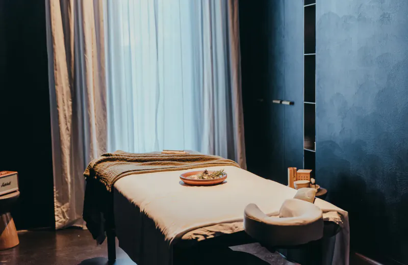 Pharomatiq Spa massage table with towels, oils, and headrest in elegant room with sheer curtains and dark walls