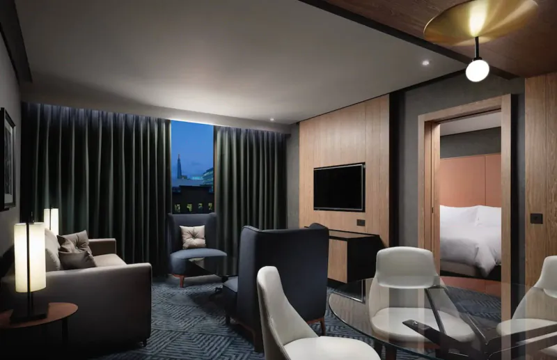 Spacious modern hotel suite at Hilton London Bankside with city skyline view, plush seating, TV, and bedroom.