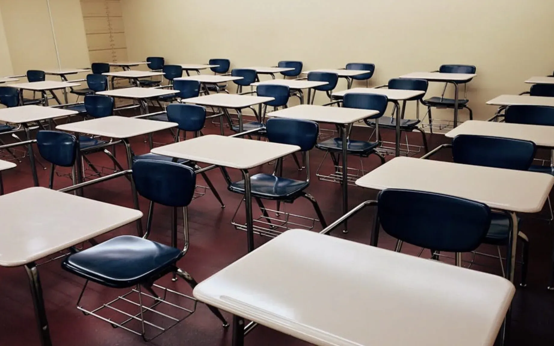 Empty classroom with rows of blue chairs at light wooden desks against beige walls