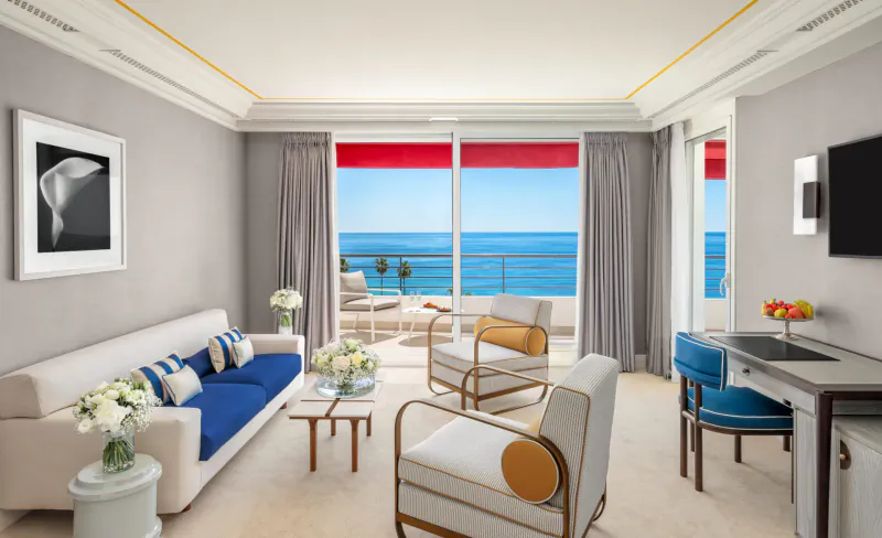 Elegant living room at Hôtel Barrière Le Majestic Cannes with white sofa, armchairs, ocean view balcony, and holiday flowers.