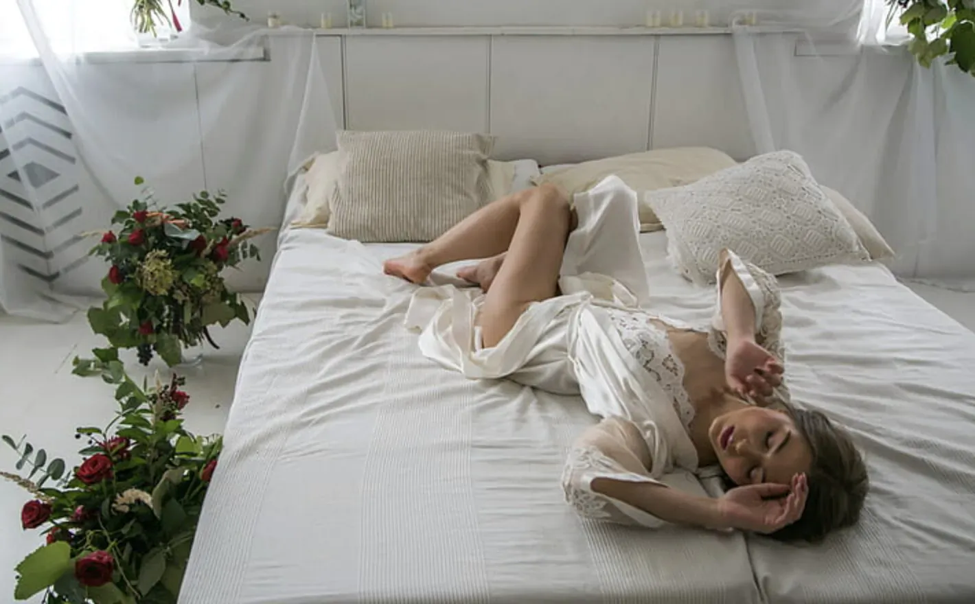 Woman in white lingerie lounging on white bed, surrounded by red roses, Valentine's Day collection